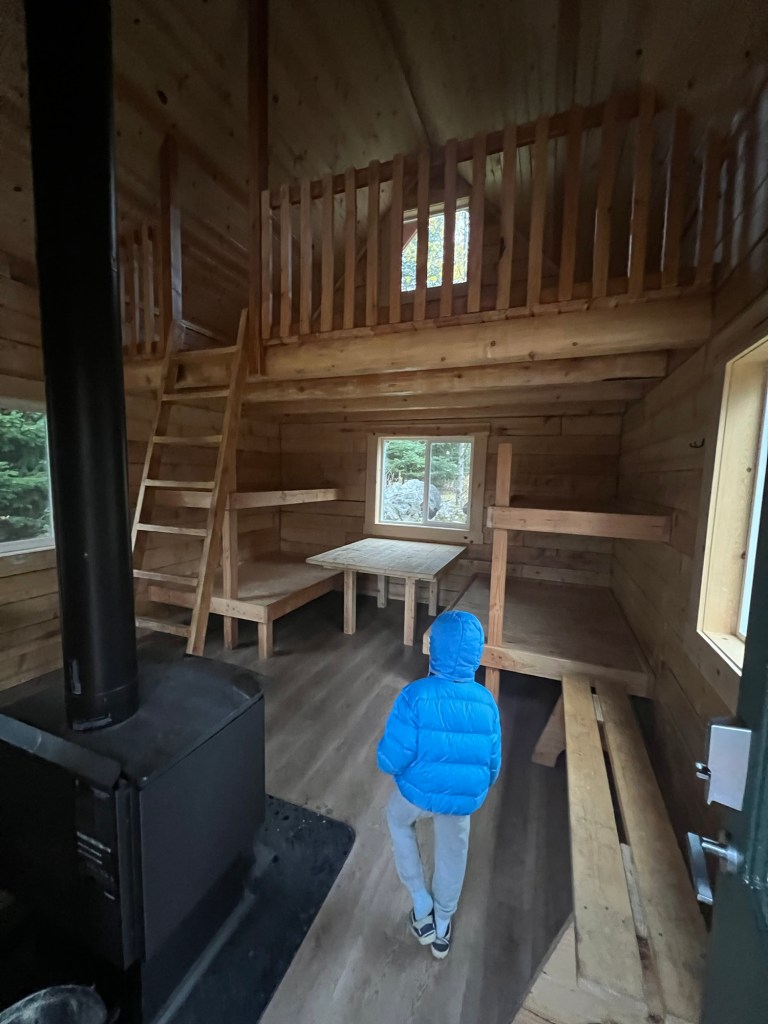 Black Bear Cabin interior with wood stove, ladder to the loft, sleeping platforms and small table